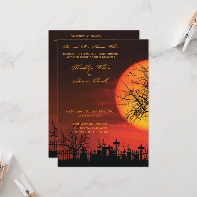 Elegant Halloween wedding invitations with a glowing orange sunset over a graveyard silhouette and bare trees, printed with gold script text.