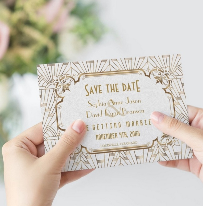 White and gold Art Deco save the date card with Gatsby-inspired geometric design held in hands.
