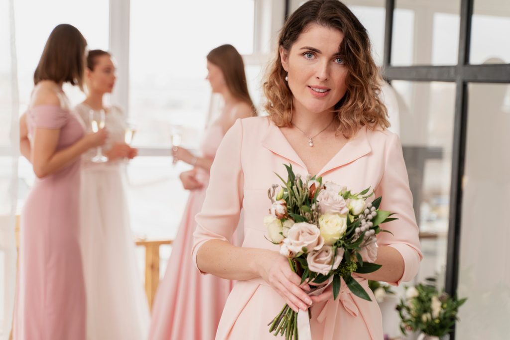 Mother of the bride in an elegant blush pink dress holding a bouquet, illustrating proper mother of the bride dress etiquette.