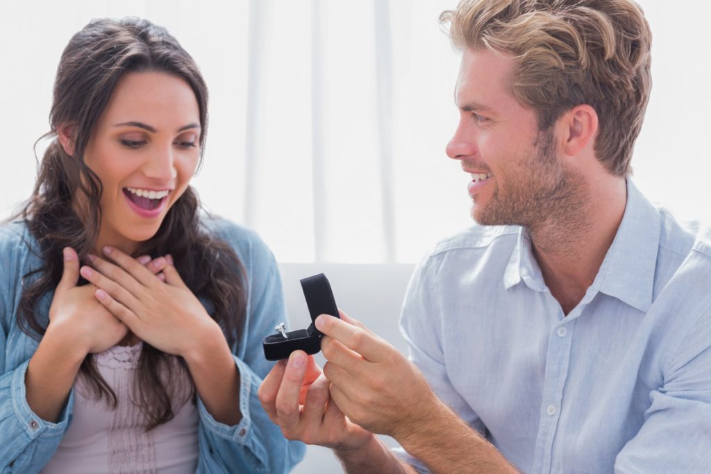 Man proposing with radiant cut moissanite engagement ring to excited woman.
