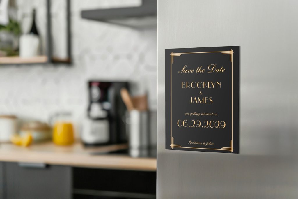 Elegant black and gold Art Deco save the date magnets displayed on a kitchen fridge.