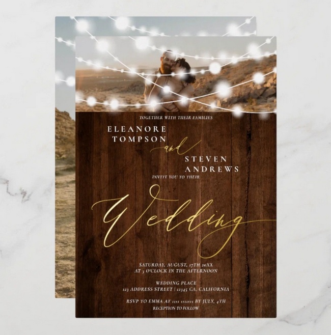 Rustic wedding invitation with string lights, wood background, and gold foil accents.