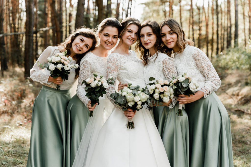 Bride with bridesmaids wearing elegant sage green bridesmaid dresses in a forest wedding setting.