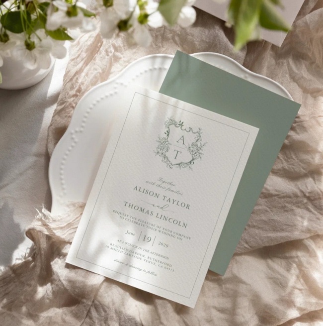 Elegant sage green wedding invitation with monogram and floral design on textured background.