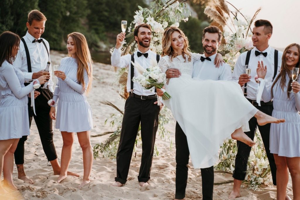 Bridal party celebrating on the beach in coordinated outfits, showcasing coastal wedding themes.